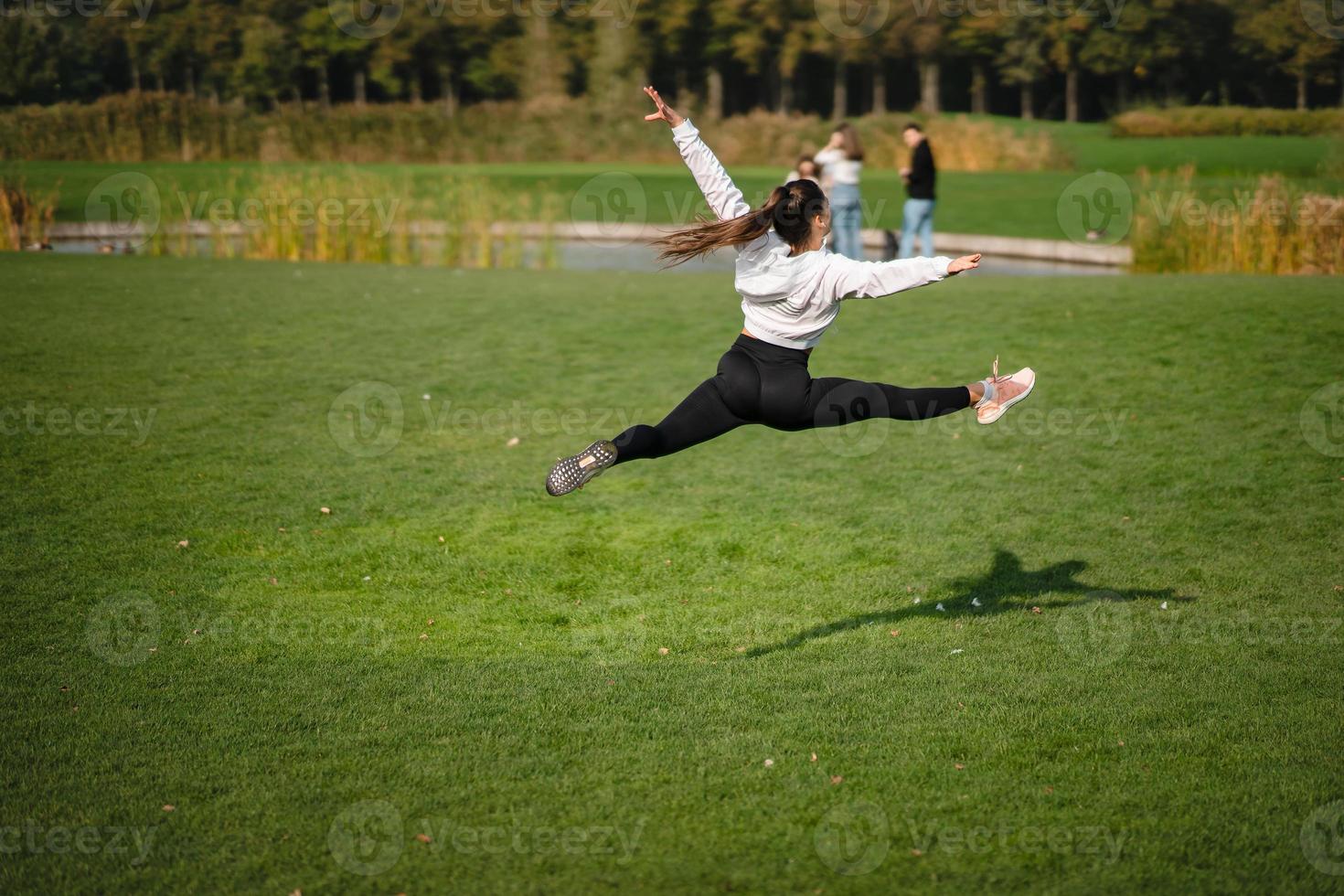 Sport girl jumping in the air on nature demonstrate perfect stretching. photo