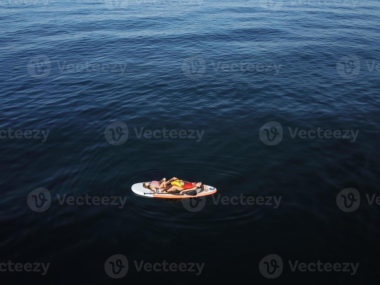 Mother with two daughters stand up on a paddle board photo