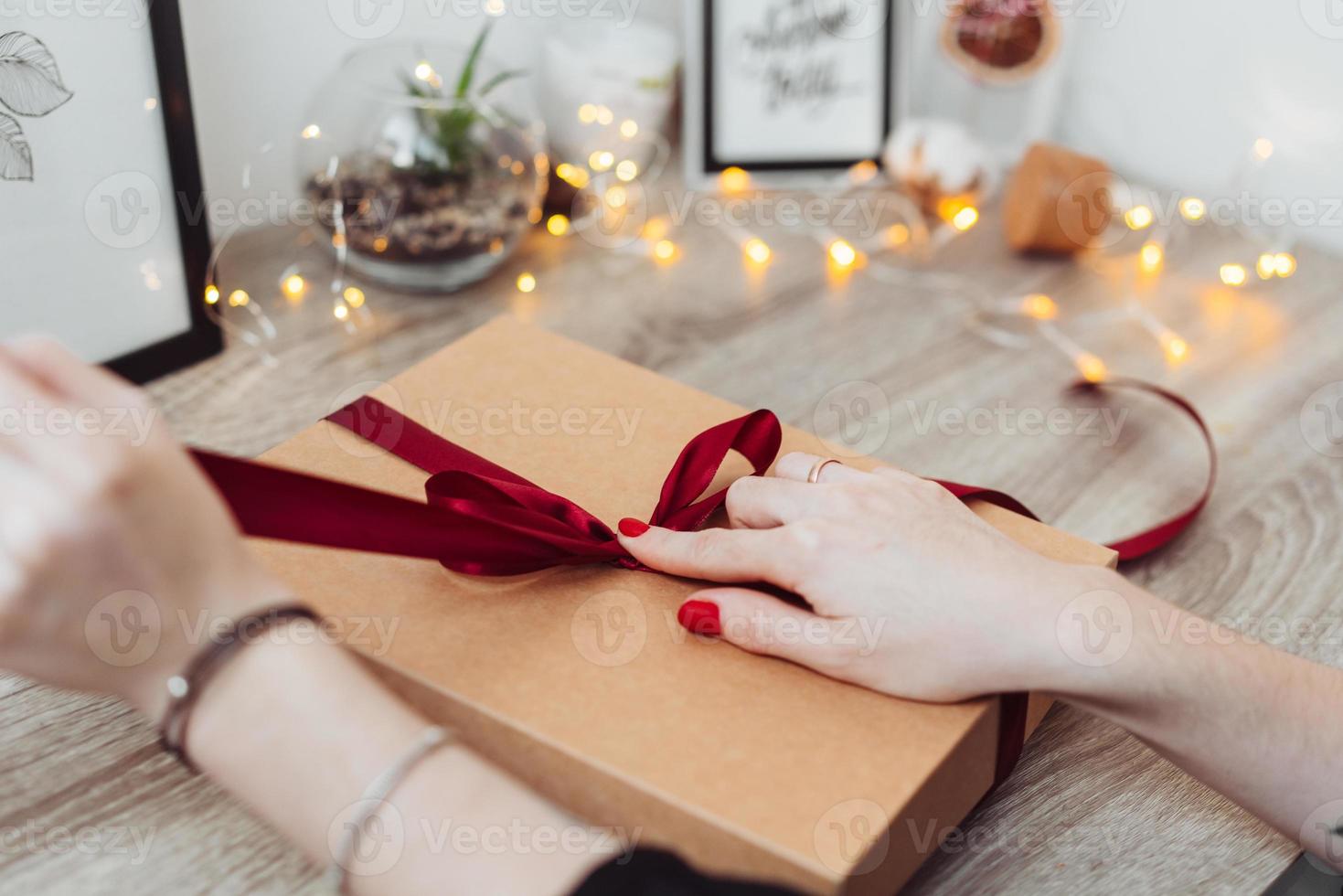 Woman wrapping present in paper with red ribbon. photo