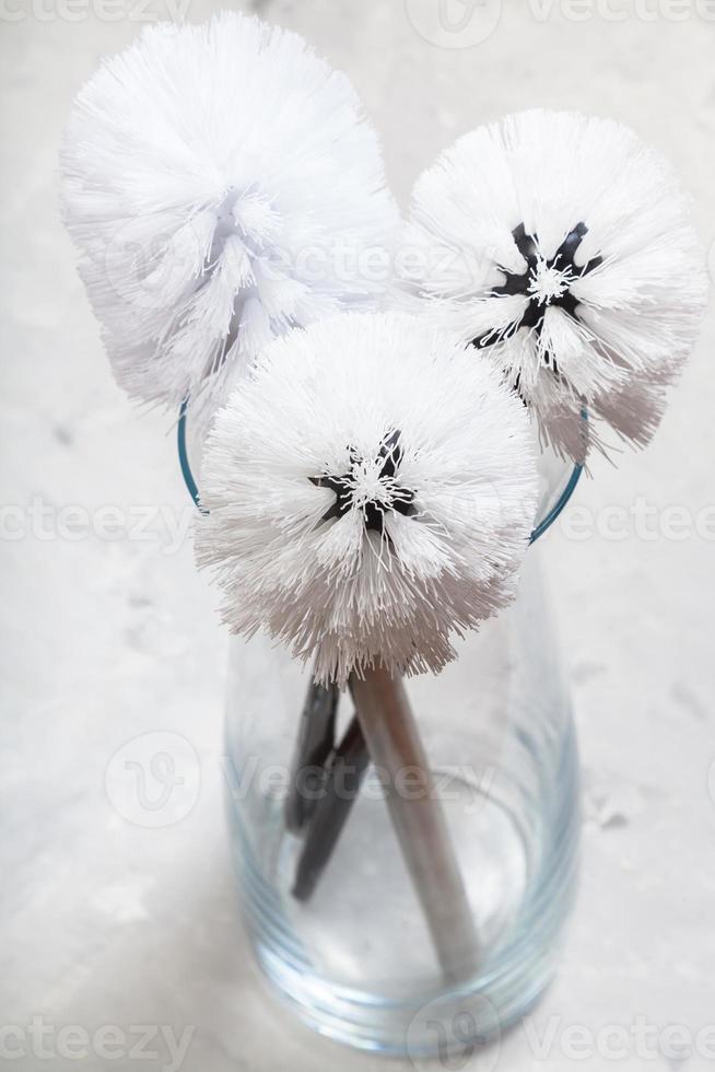 bunch of toilet brushes in glass vase on concrete photo
