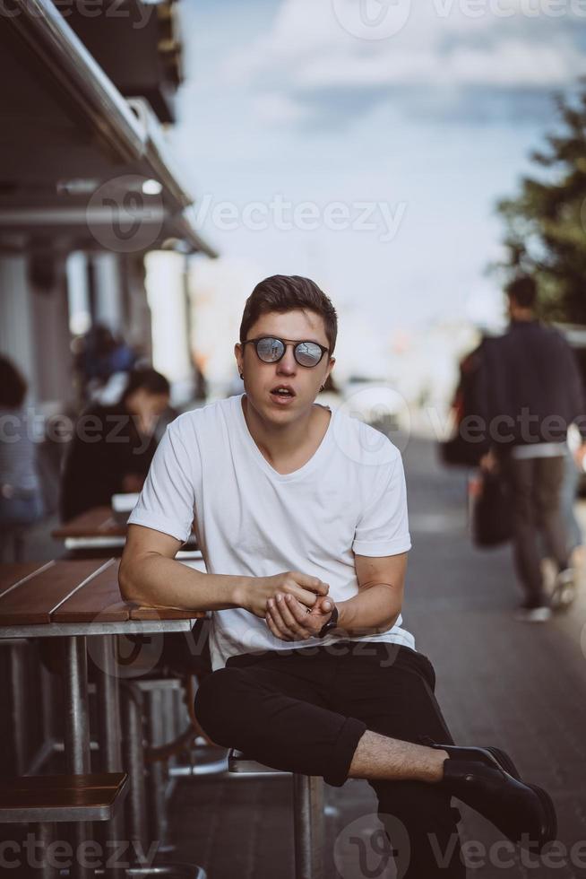 chico sentado en la calle de la ciudad, mira la cámara y alrededor foto