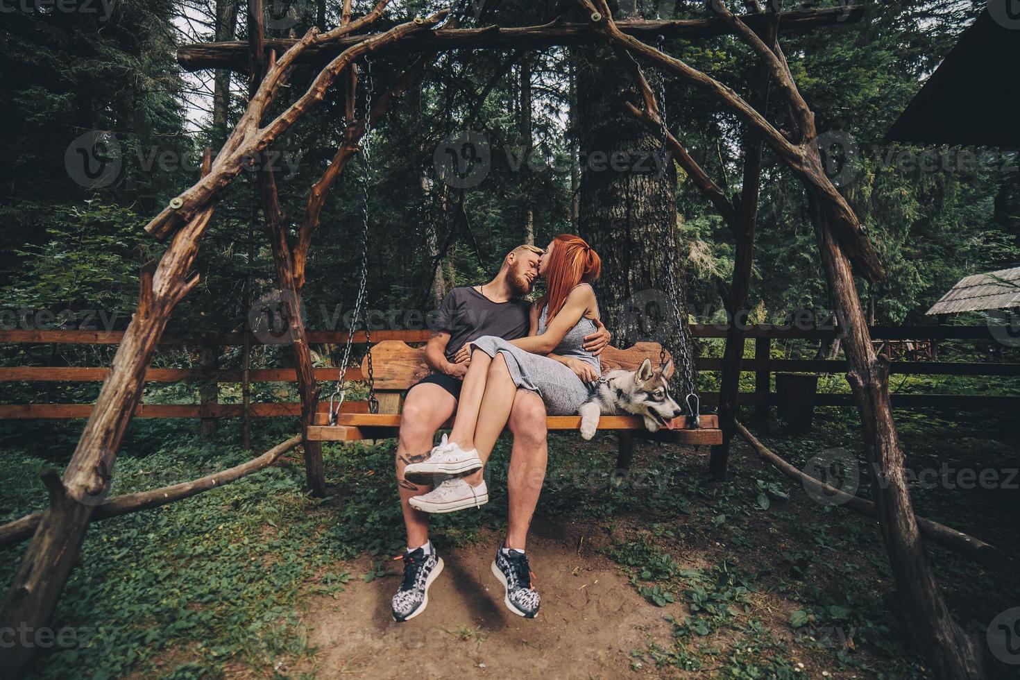 beautiful couple together with dog on a swing photo