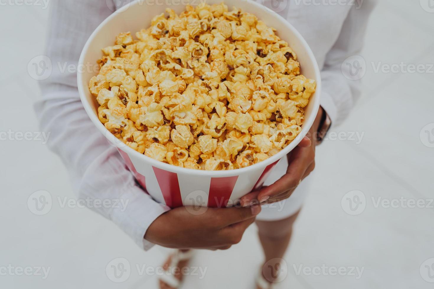 Close-up photo of a young sweet girl, who is holding a tube of popcorn in her hands.