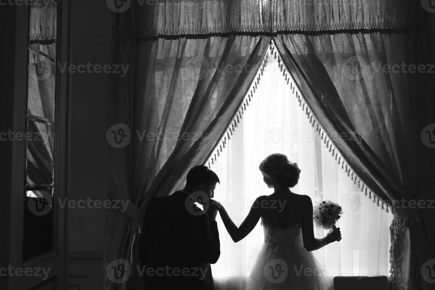 bride and groom standing in front of window photo