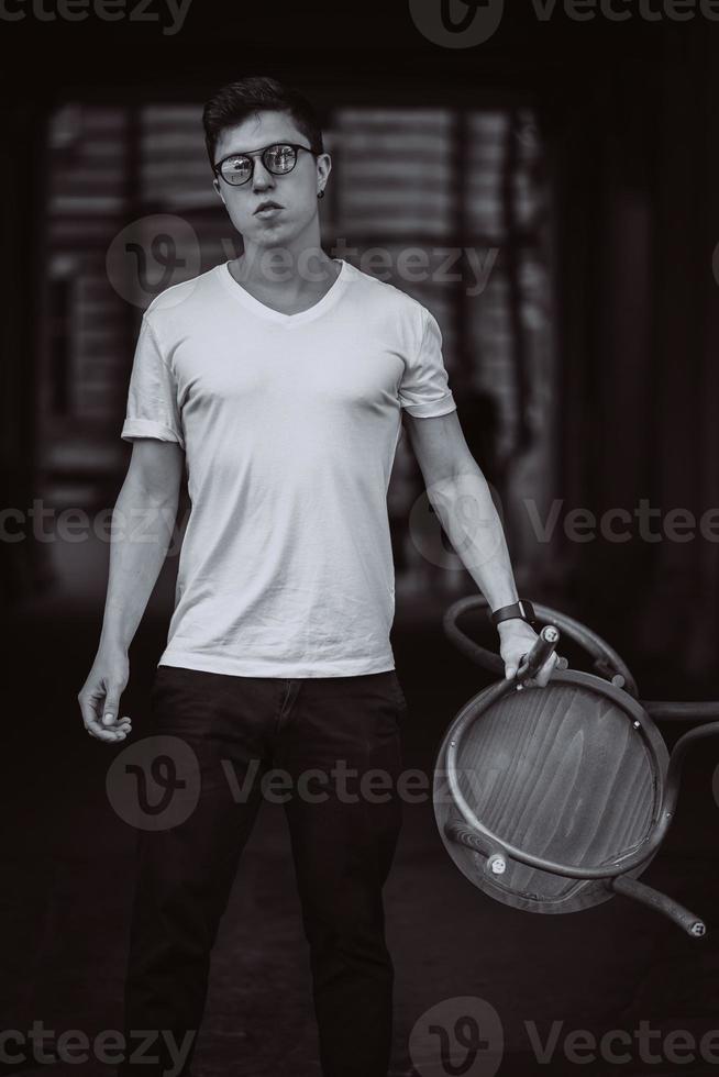 portrait of men standing with chair in white t-shirt and sunglasses in the street photo