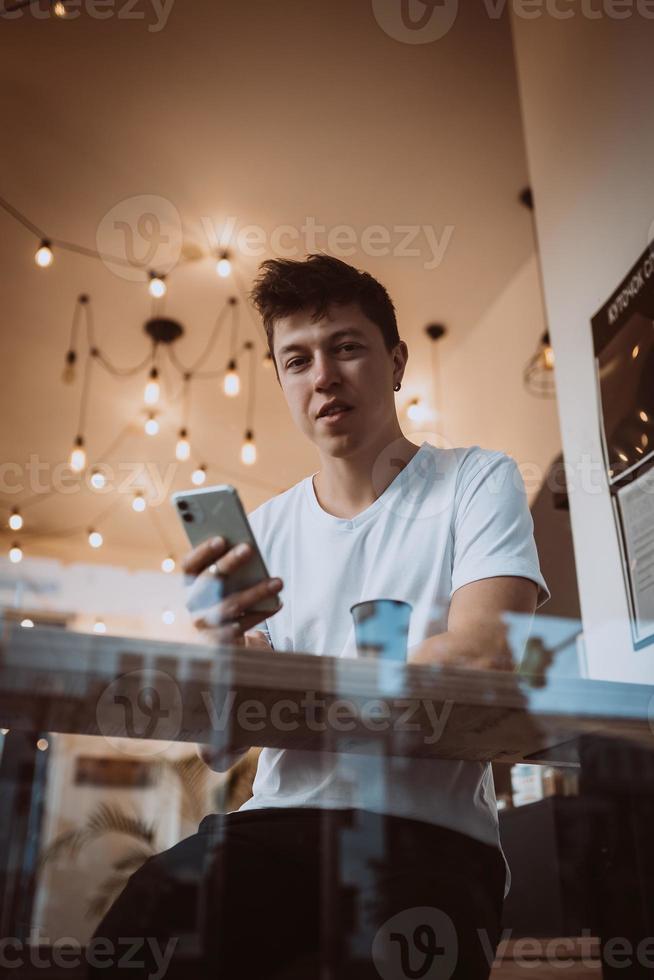 un hombre joven y guapo usa un teléfono inteligente en un café. foto detrás de un cristal
