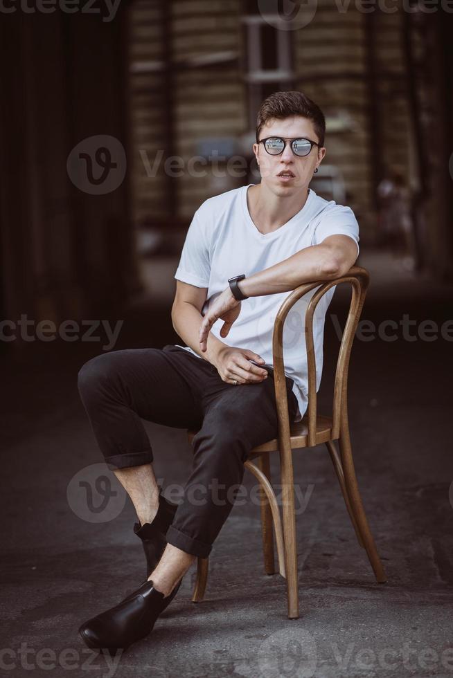 portrait of men sitting on chair with white t-shirt and sunglasses in the street photo
