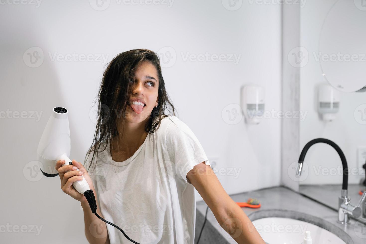 Young beautiful woman in the bathroom holding a hairdryer photo