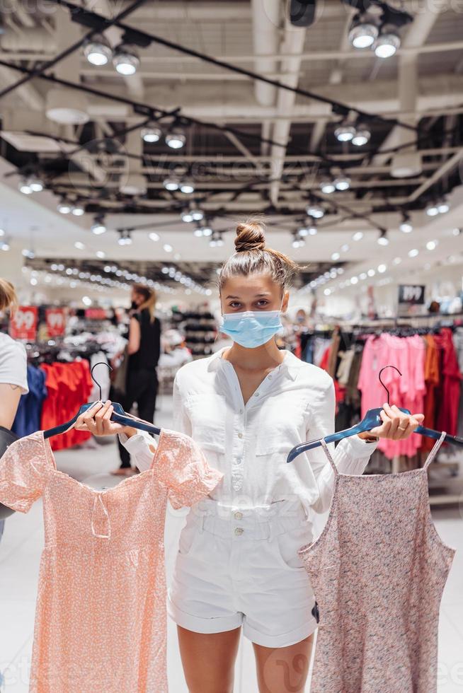 Young woman shopping apparels in clothing boutique with protective face mask photo