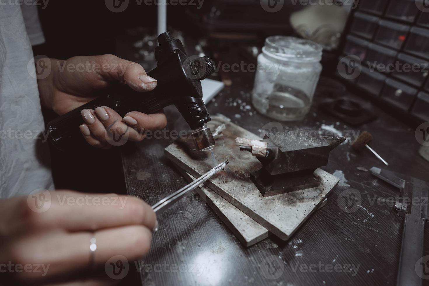 In the workshop, a woman jeweler is busy soldering jewelry photo