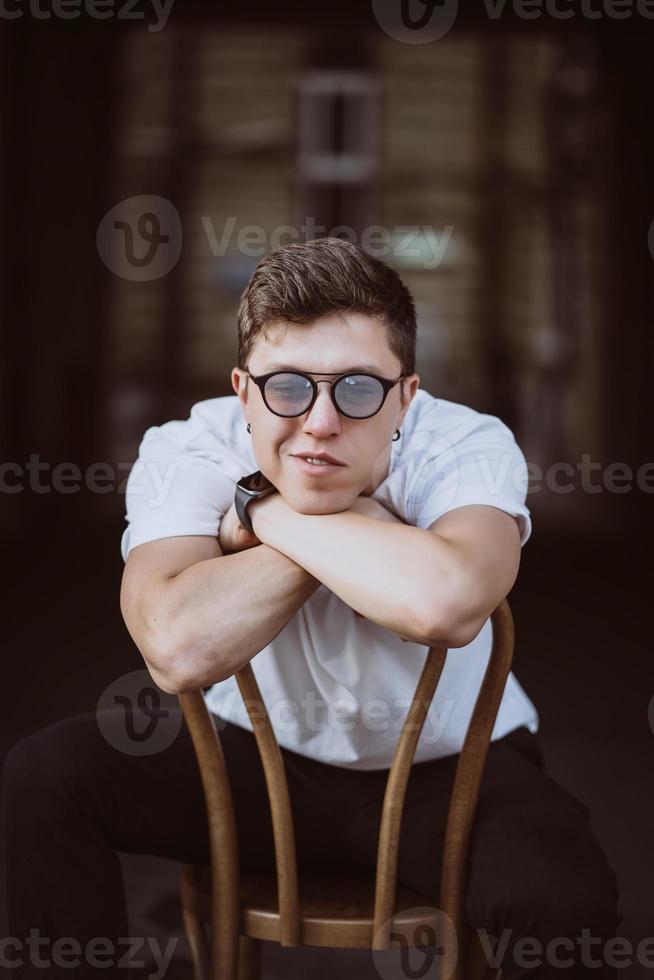 portrait of men sitting on chair with white t-shirt and sunglasses in the street photo