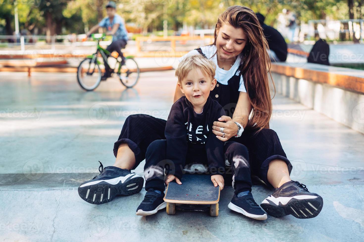 joven madre le enseña a su hijo pequeño a andar en patineta foto