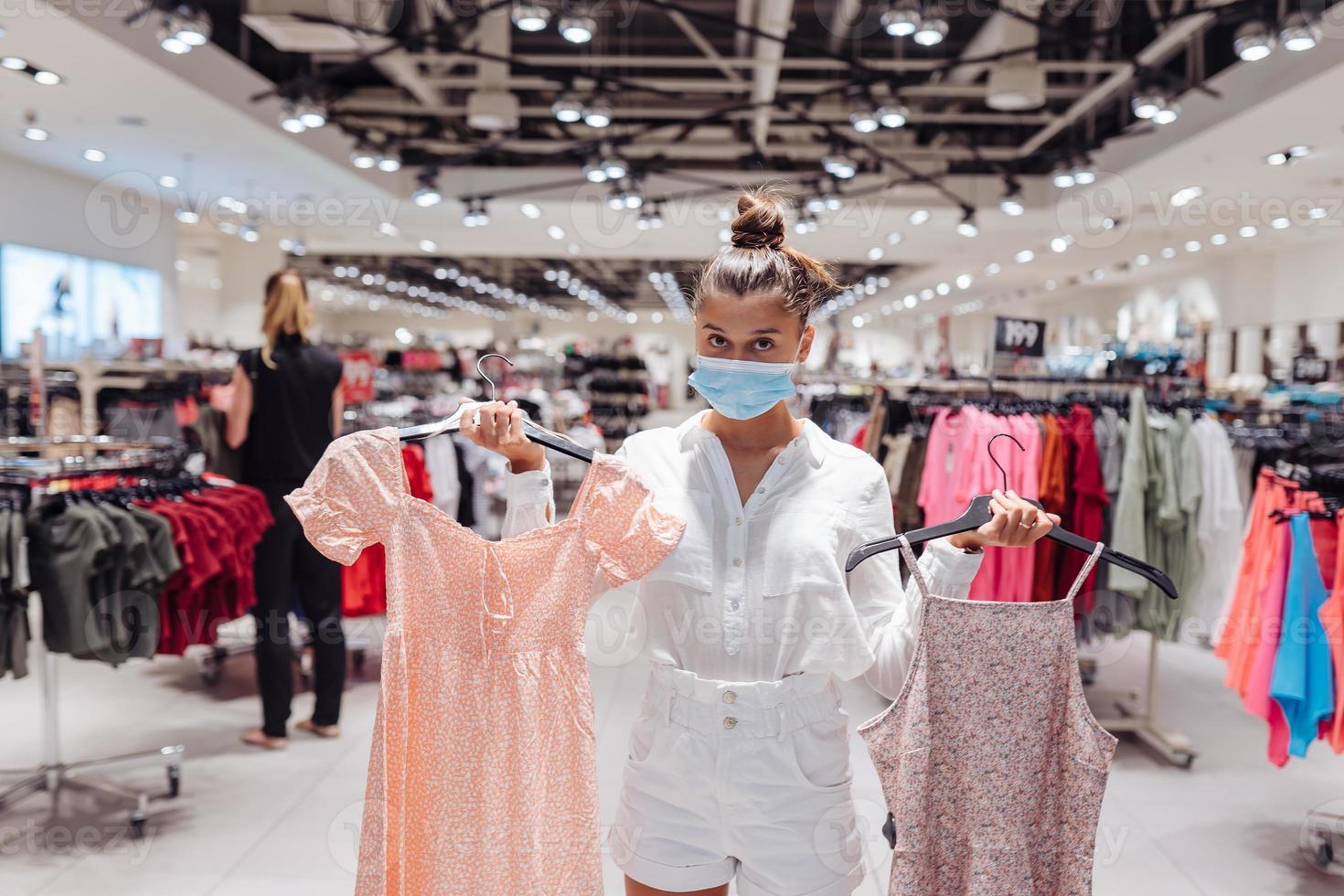 Young woman shopping apparels in clothing boutique with protective face mask photo