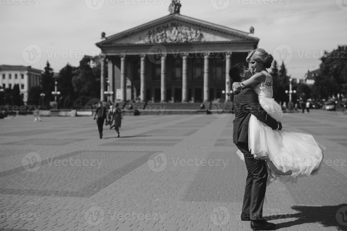 el novio sostiene a la novia en sus brazos y la retuerce foto