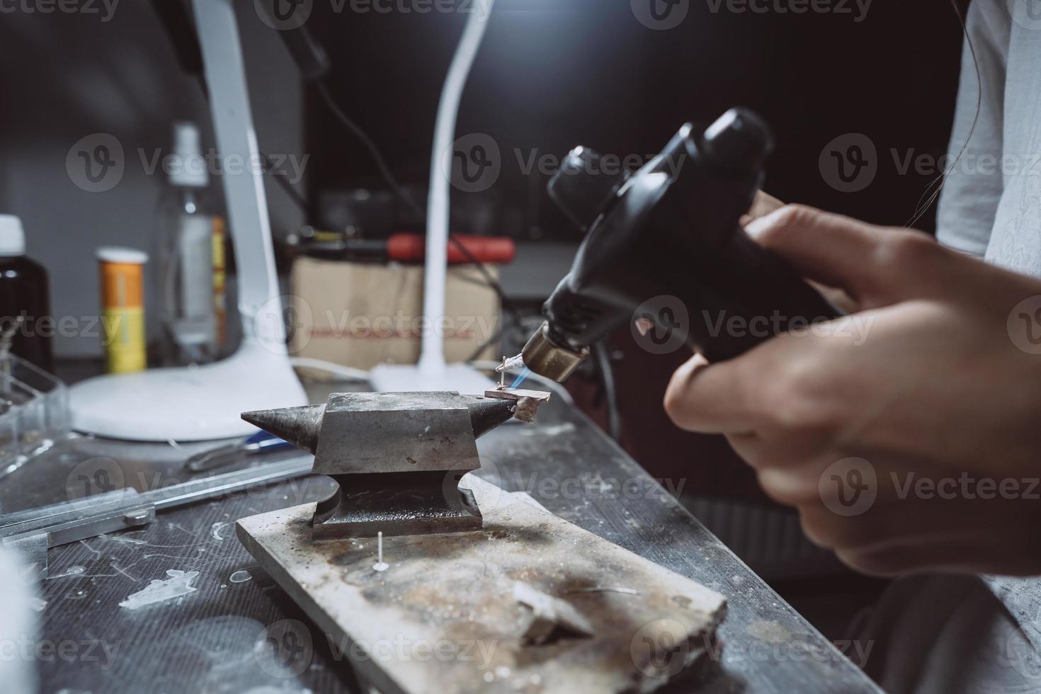 In the workshop, a woman jeweler is busy soldering jewelry photo