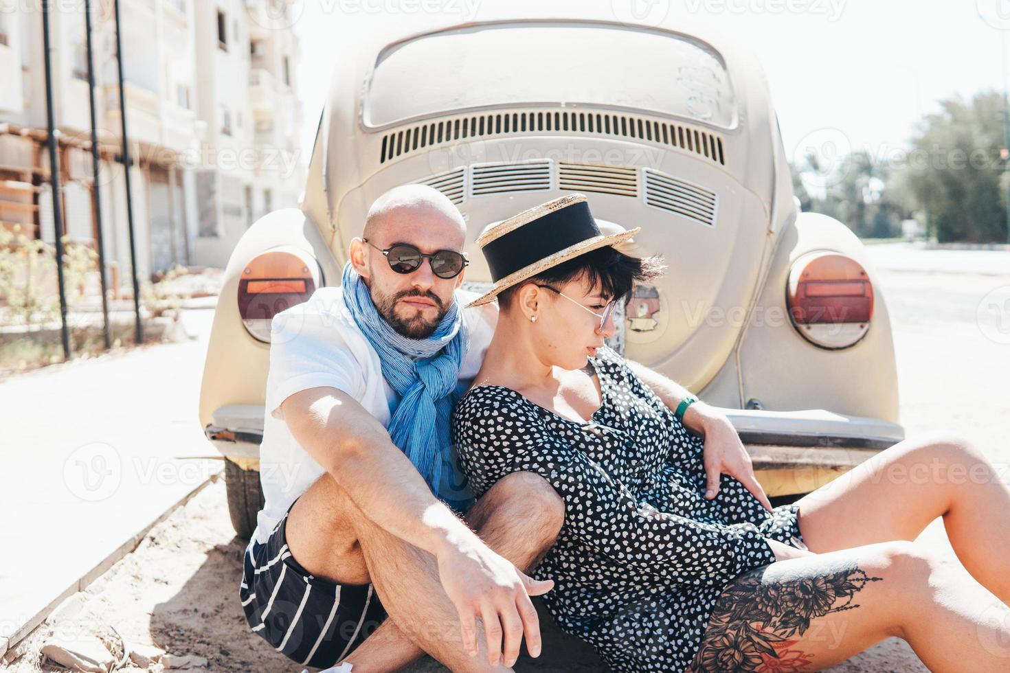 Couple sitting on the asphalt behind the car photo