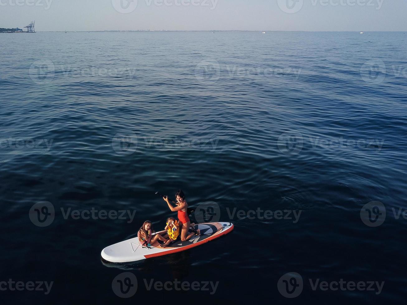 Mother with two daughters stand up on a paddle board photo