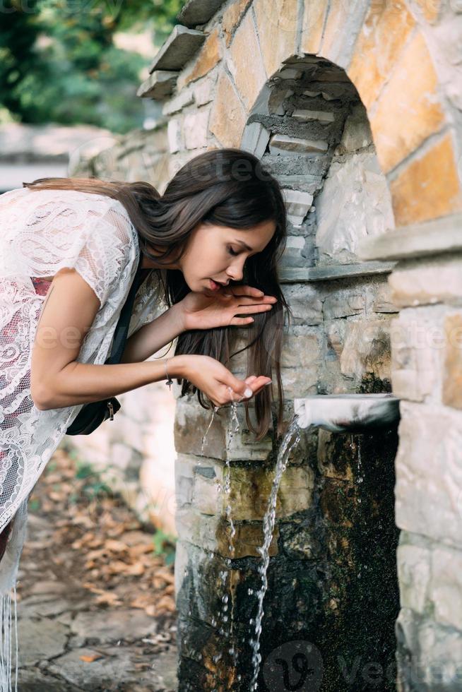 Beautiful, young girl drinks spring water outdoor photo