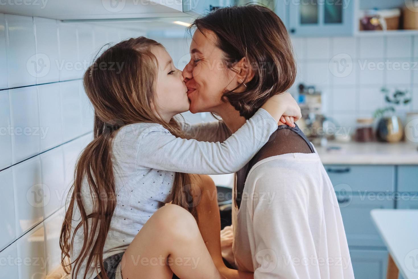 mamá besa a su pequeña hija en la cocina foto