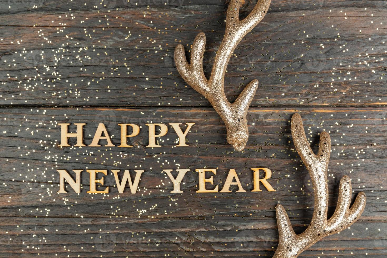 tarjeta de felicitación de feliz año nuevo con texto de madera y cuernos de venado dorado. fondo festivo foto