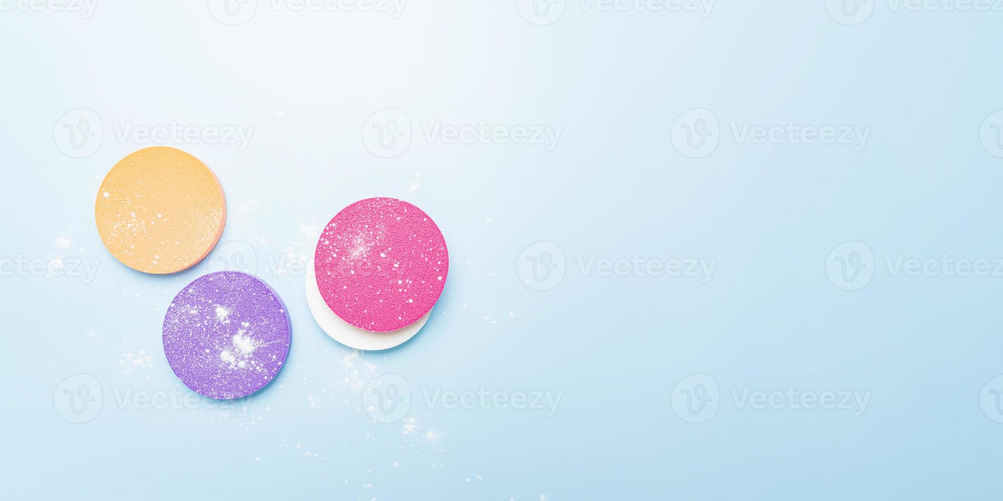 Cosmetic sponges and dusted transparent mineral powder on a blue background. The concept of makeup, face cosmetics, skin care. Minimalism, top view. Banner photo