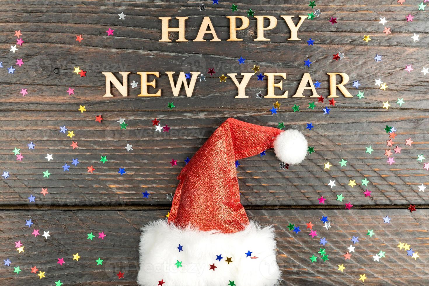 Happy new year 2023 wooden letters quote with red sparkling santa hat on wooden table with glitter. Festive greeting card for a new year celebration photo