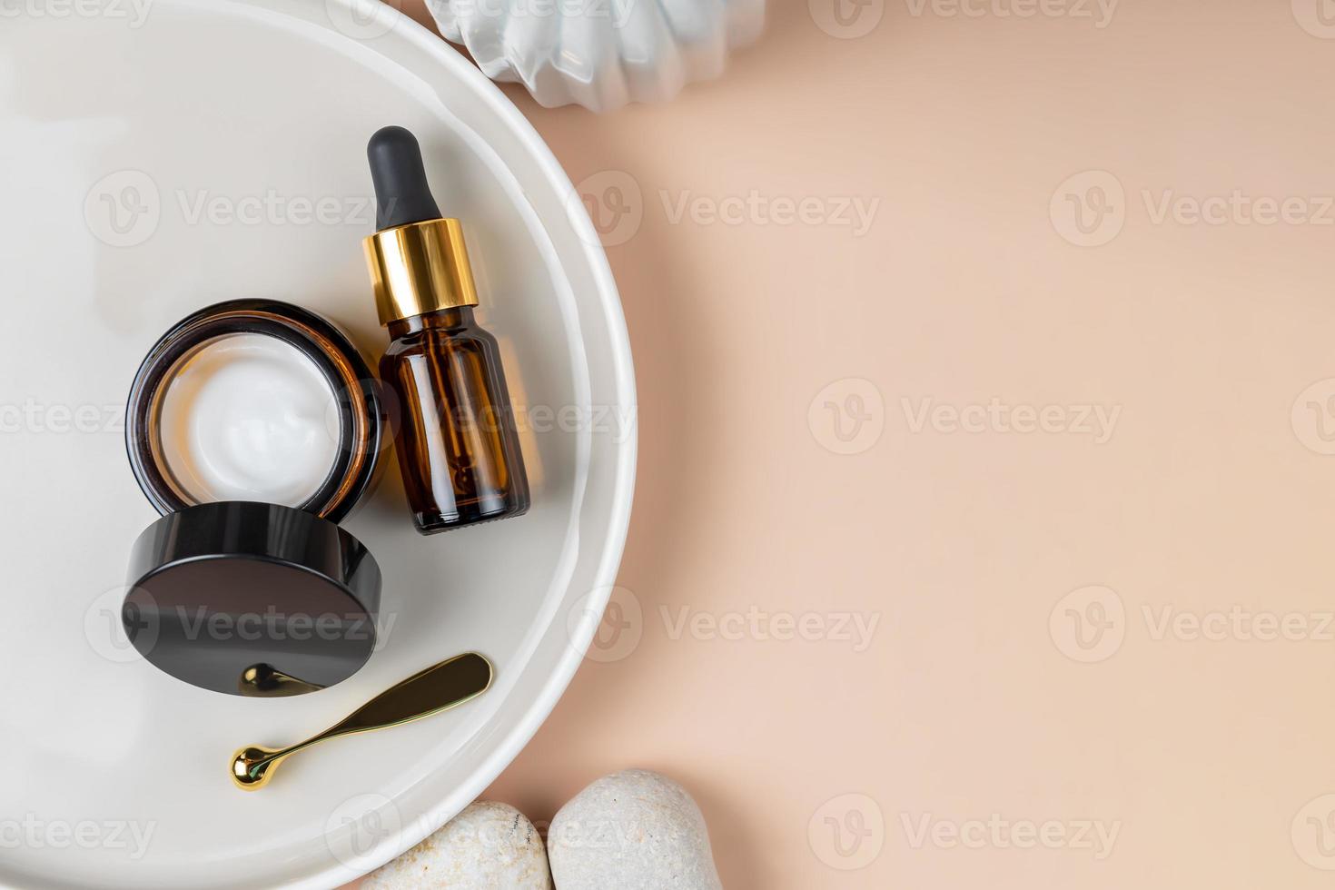 Amber glass containers with natural cosmetics and spatula for applying cream on ceramic tray on a beige background. SPA organic bio cosmetics set. Copy space photo