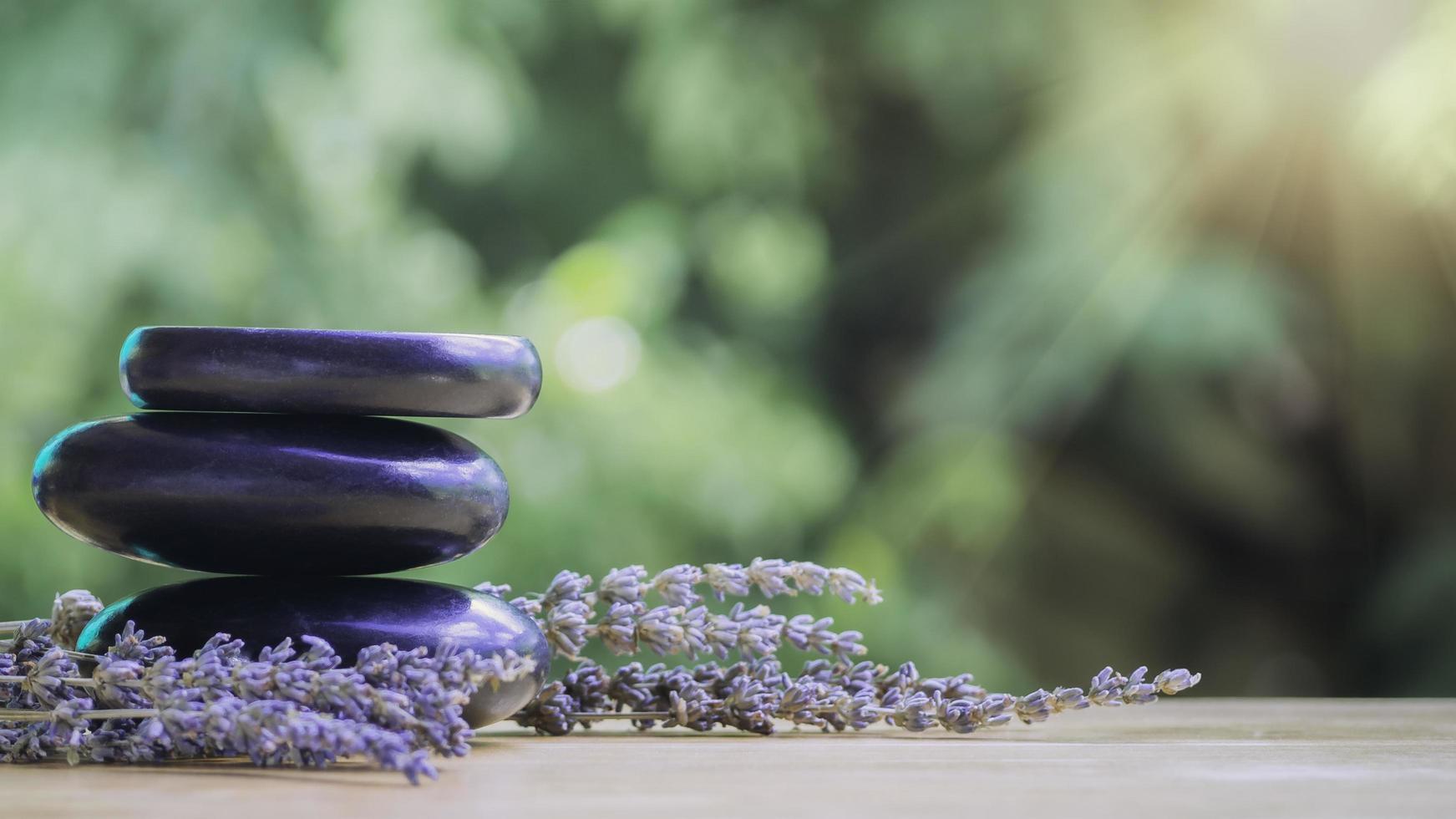 Balance and wellness or health concept with pile of black spa stones on wood and spikes of flowering lavender with aromatherapy. Side view and landscape composition feel relaxed. photo