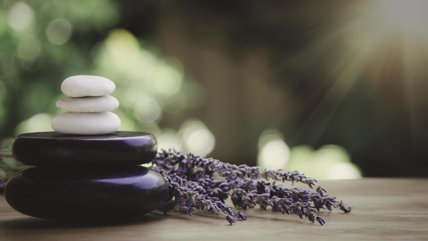 concepto de equilibrio y bienestar o salud con un montón de piedras de spa negras sobre madera y espigas de lavanda floreciente con aromaterapia. la vista lateral y la composición del paisaje se sienten relajadas. foto