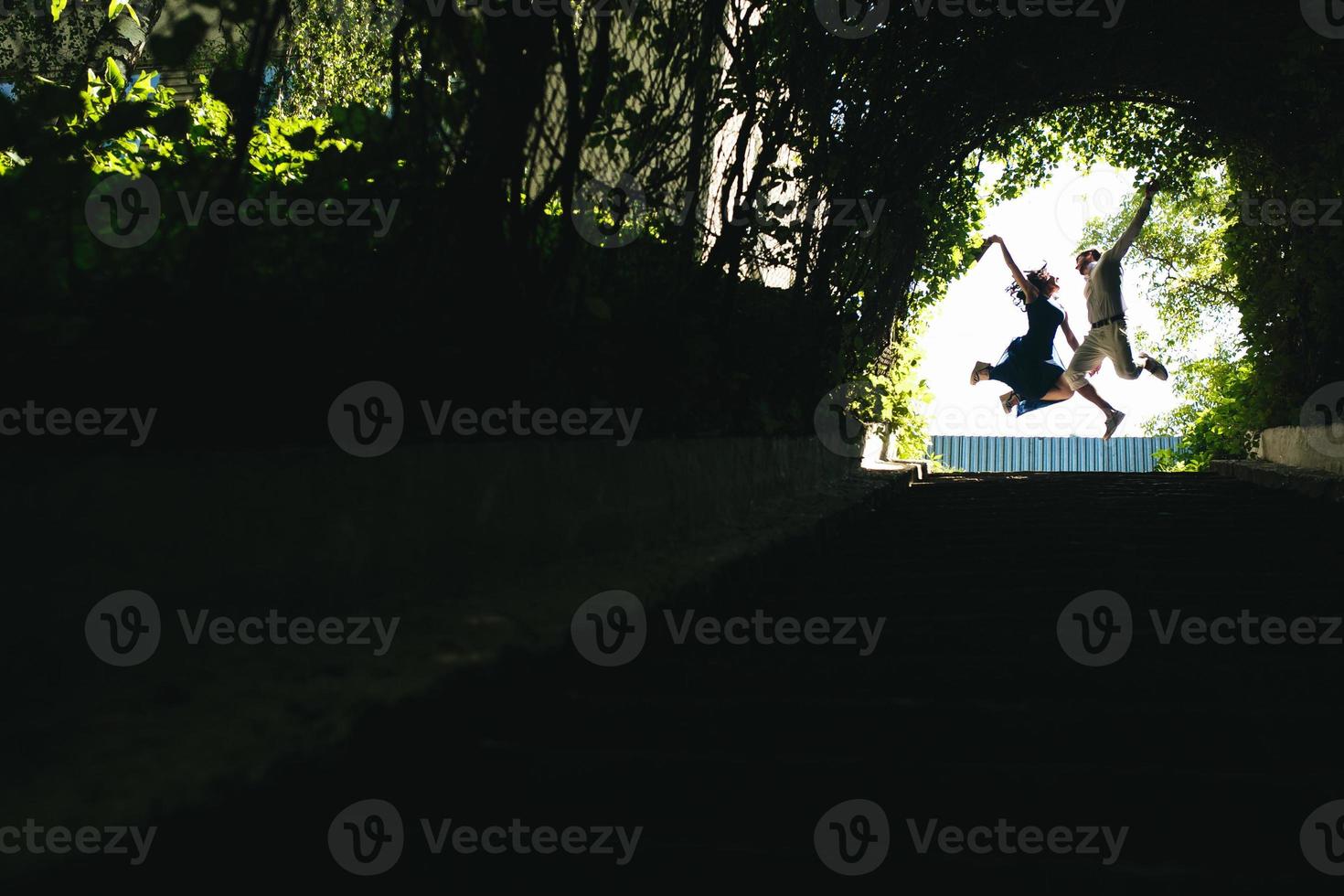 couple jumping in the end of tunnel with trees photo