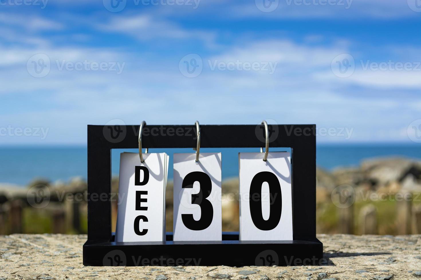 Texto de la fecha del calendario del 30 de diciembre en un marco de madera con un fondo borroso del océano. foto