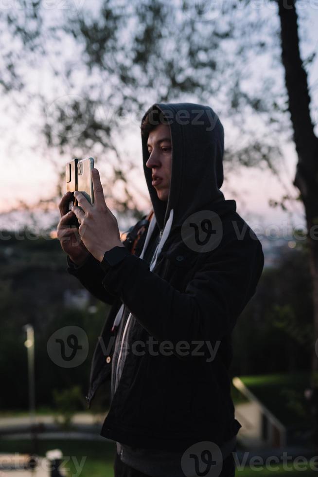 Young guy in the park takes a photo on two smartphones