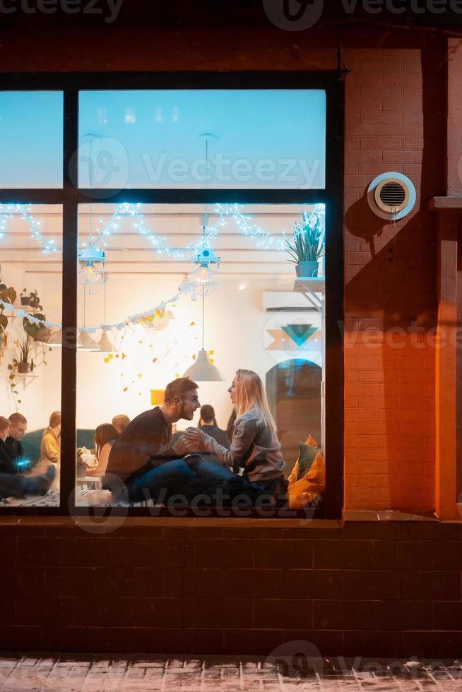 Photo through window. Young couple in cafe with stylish interior