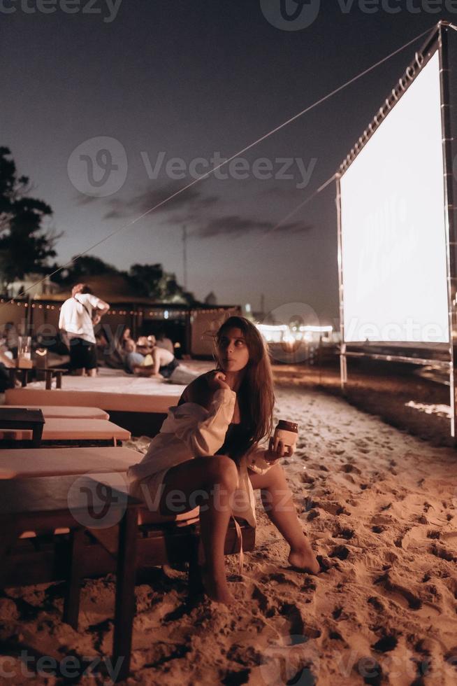 mujer joven está sentada en una silla en la playa de noche foto