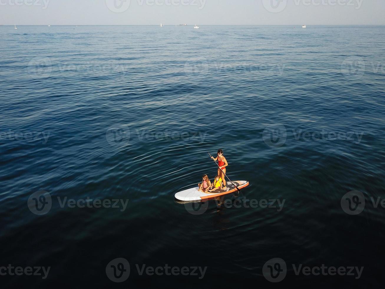 Mother with two daughters stand up on a paddle board photo