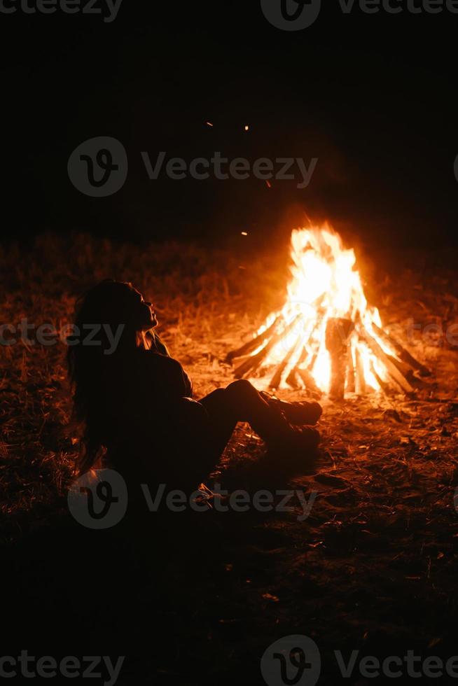 mujer sentada y calentándose cerca de la hoguera en el bosque nocturno. foto