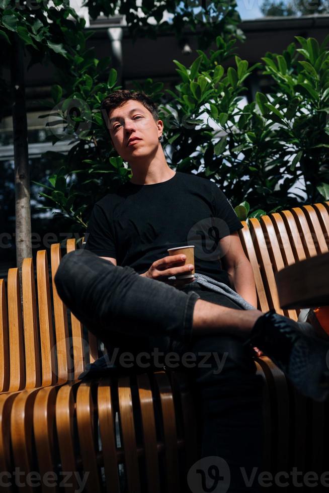 joven sosteniendo una bebida para llevar mientras se sienta en un banco de madera foto