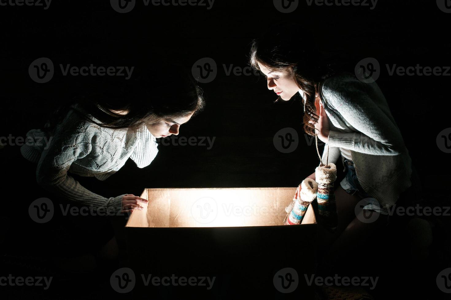 Sisters opens a box with a Christmas present and fascinated looks inside photo