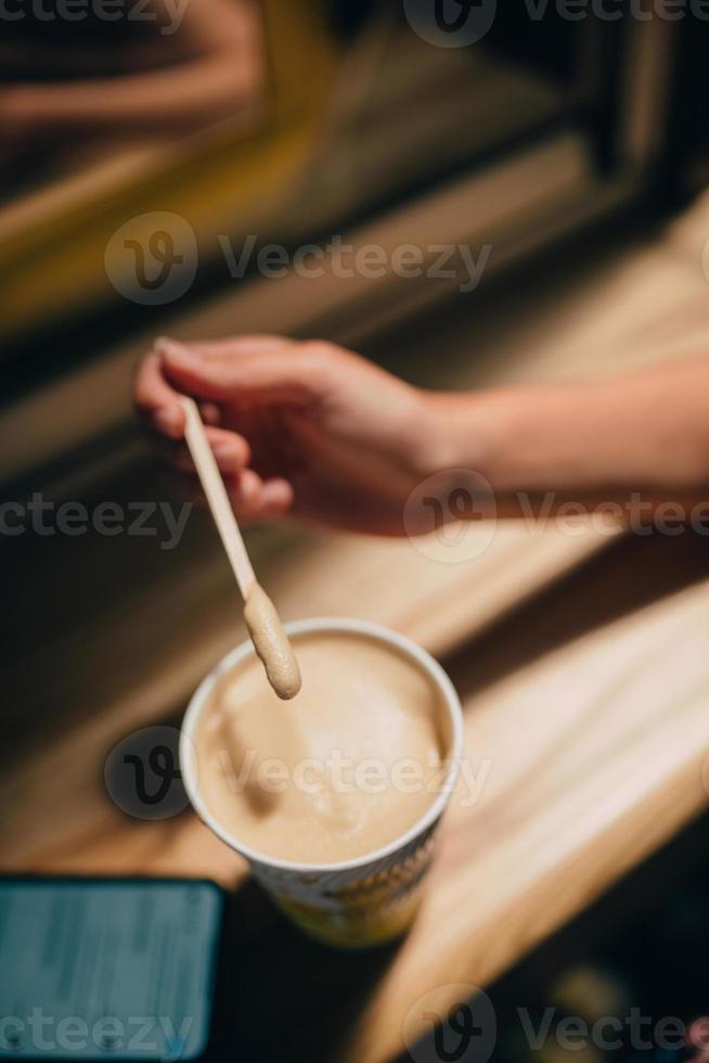 A female hand holding a stick over a latte paper mug photo