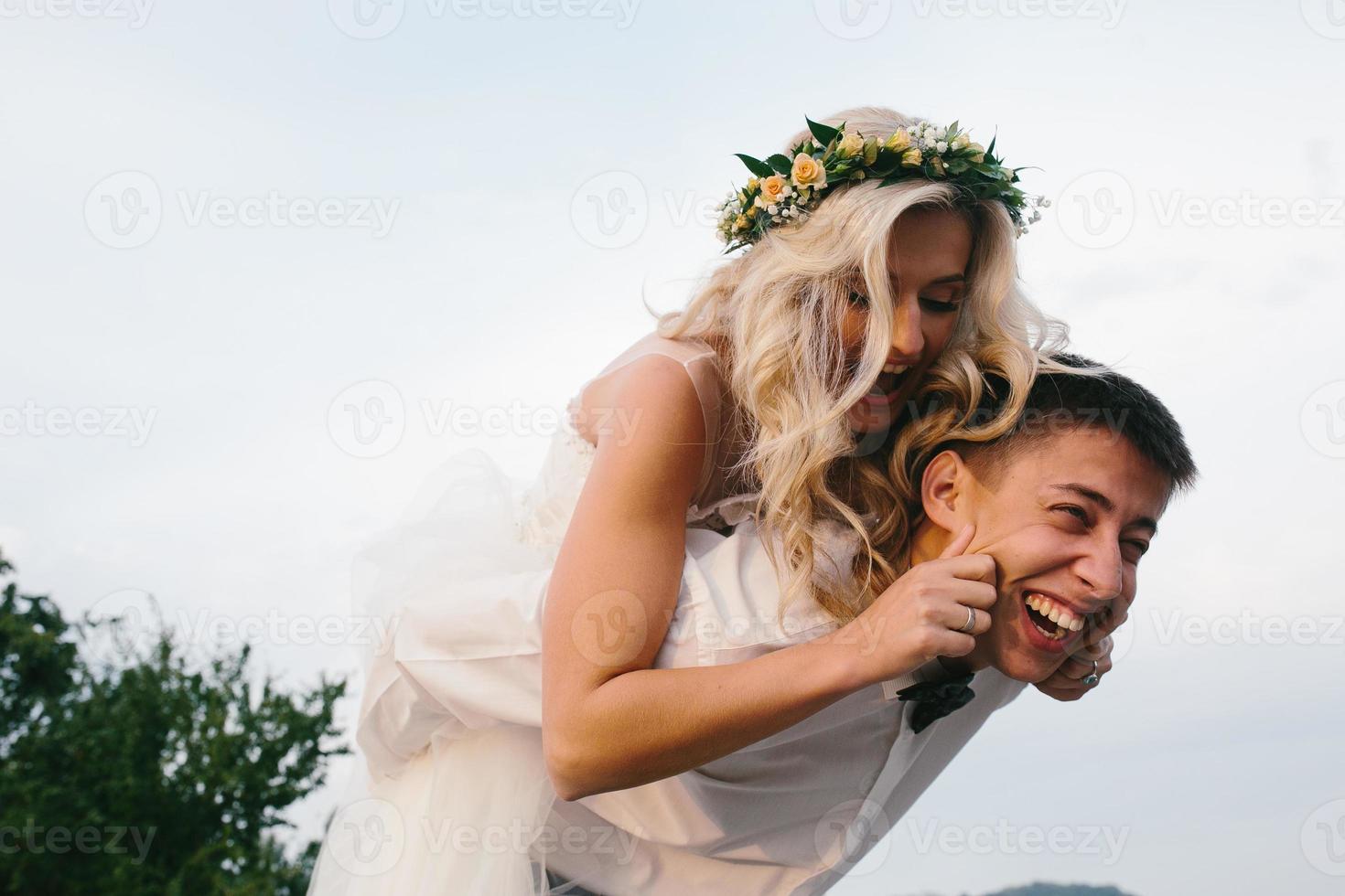 groom carries bride on his back outdoors photo