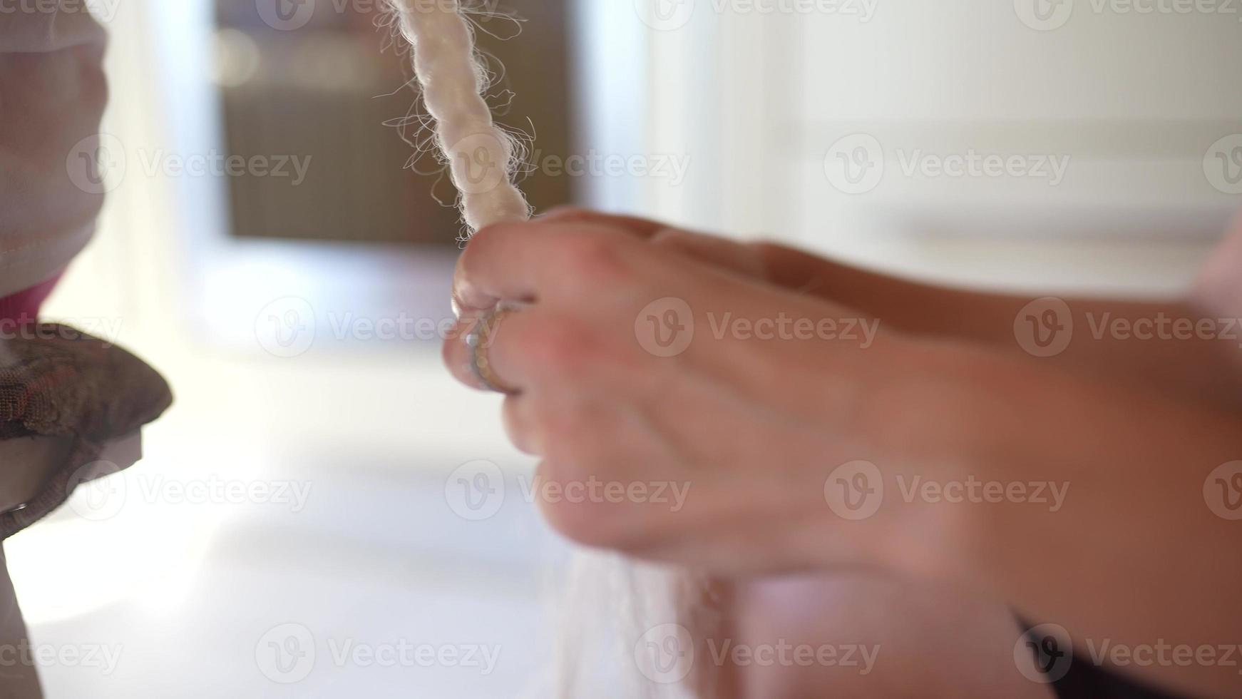 A female hairdresser weaves a braid from a white kenekalon. Close up of the process photo