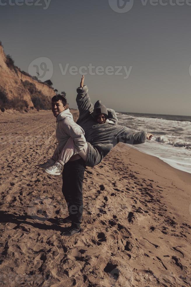 el hombre lleva a su novia en la espalda, pareja divirtiéndose en la orilla del mar foto