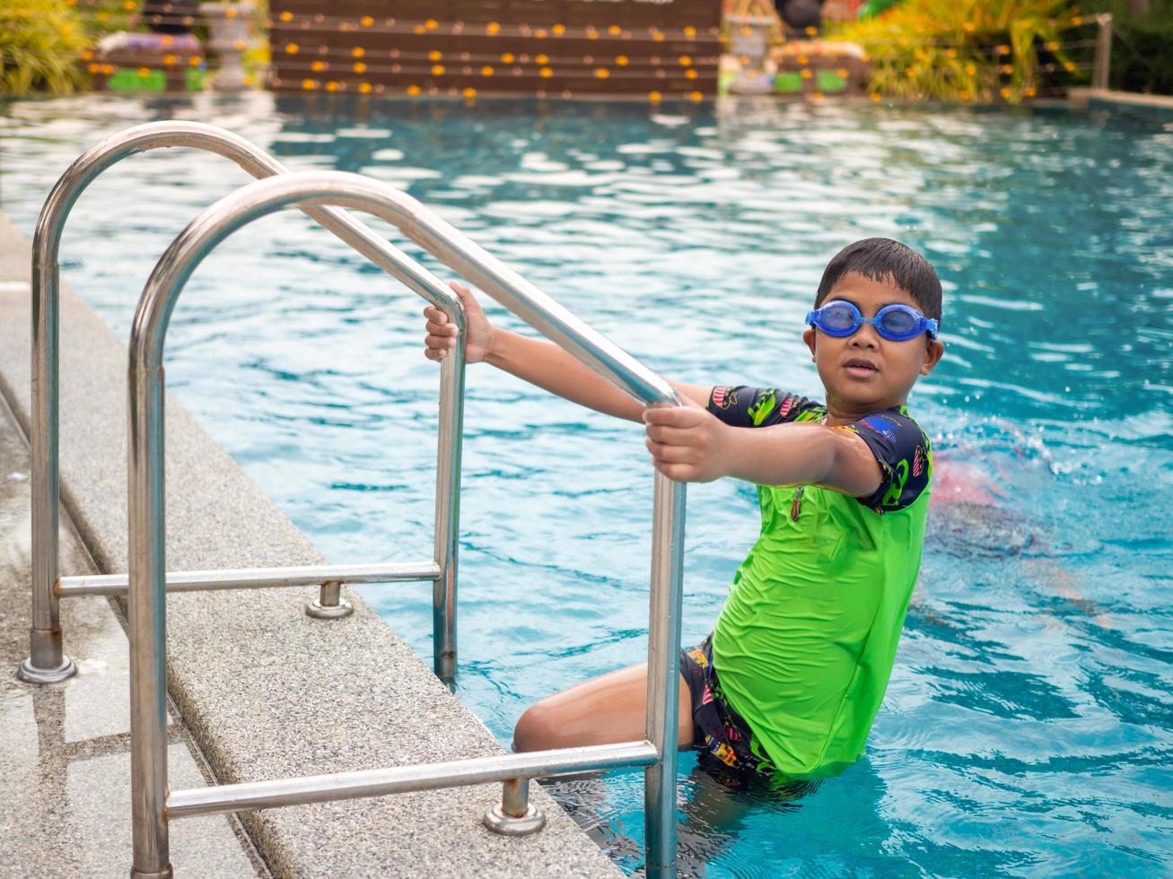 The boy wearing swimming goggles on blue pool ladder green swimsuit photo