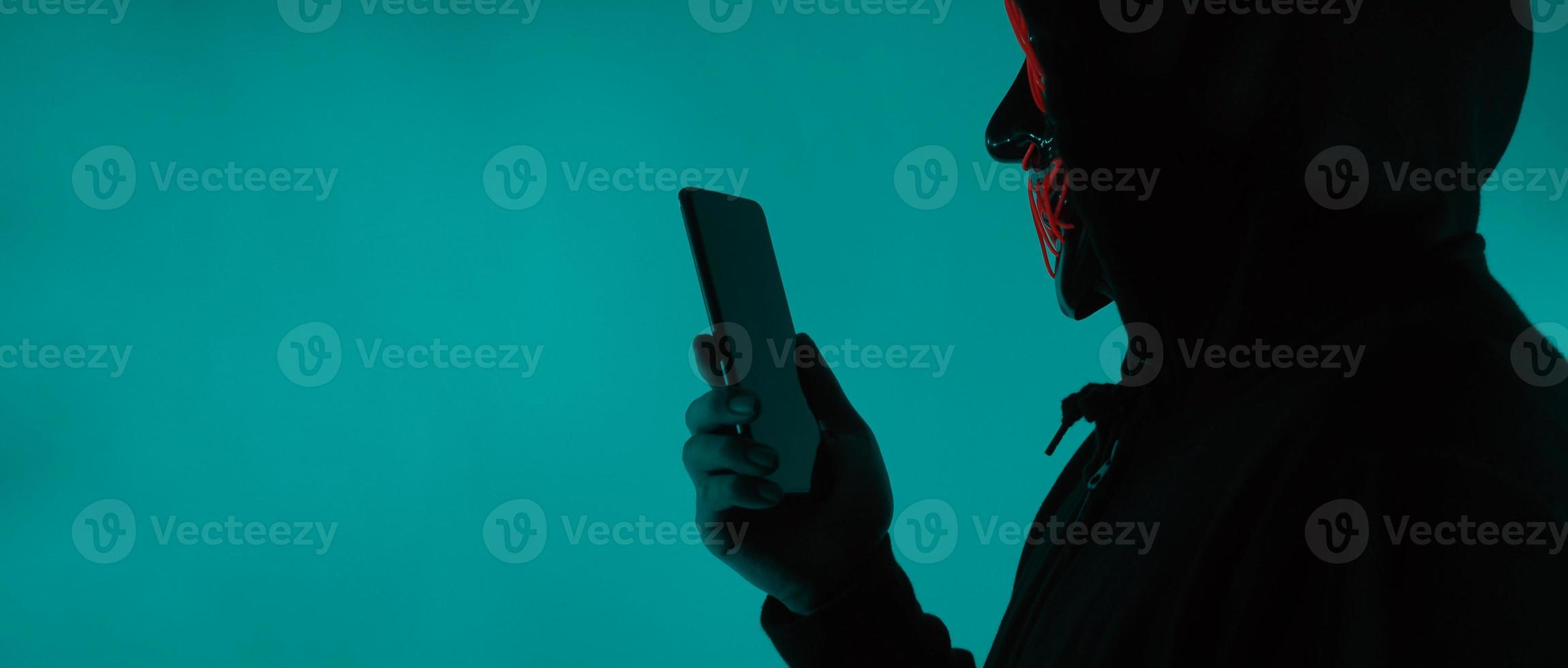 Anonymous hacker and face mask with smartphone in hand. photo