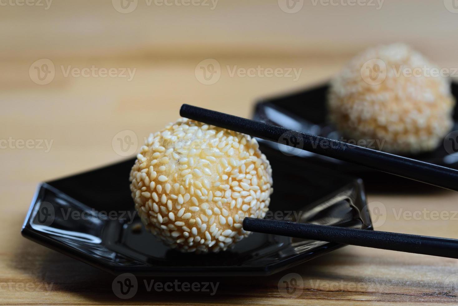 Close up of fresh deep fried sesame balls or jian dui lying on dark plates against a light background with chopsticks photo