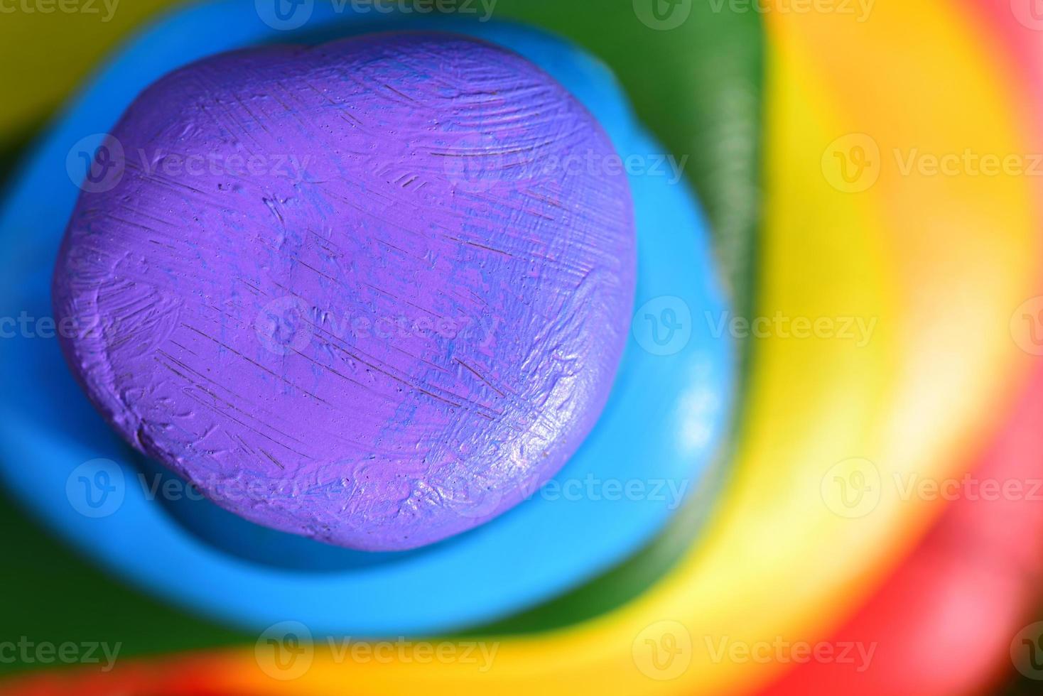 Several brightly colored pebbles that have been painted in rainbow colors lie on top of one another and form a background photo