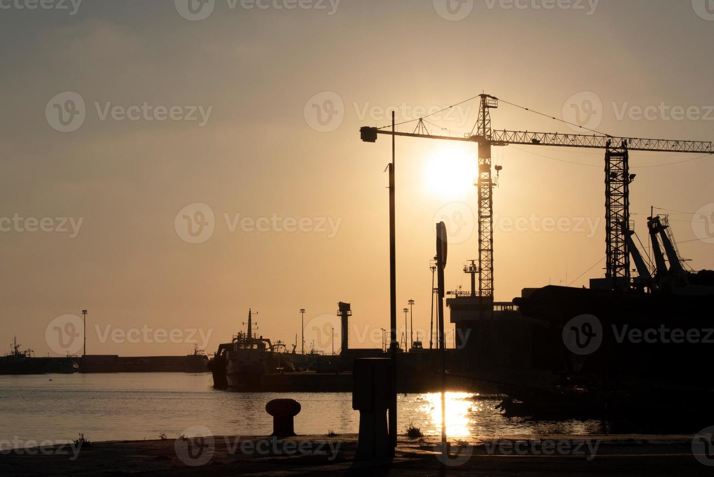 January 4th, 2021, in Mazara del Vallo, Sicily, the sun sets behind the port in the evening and shines a red light on the ships in front of the sea photo