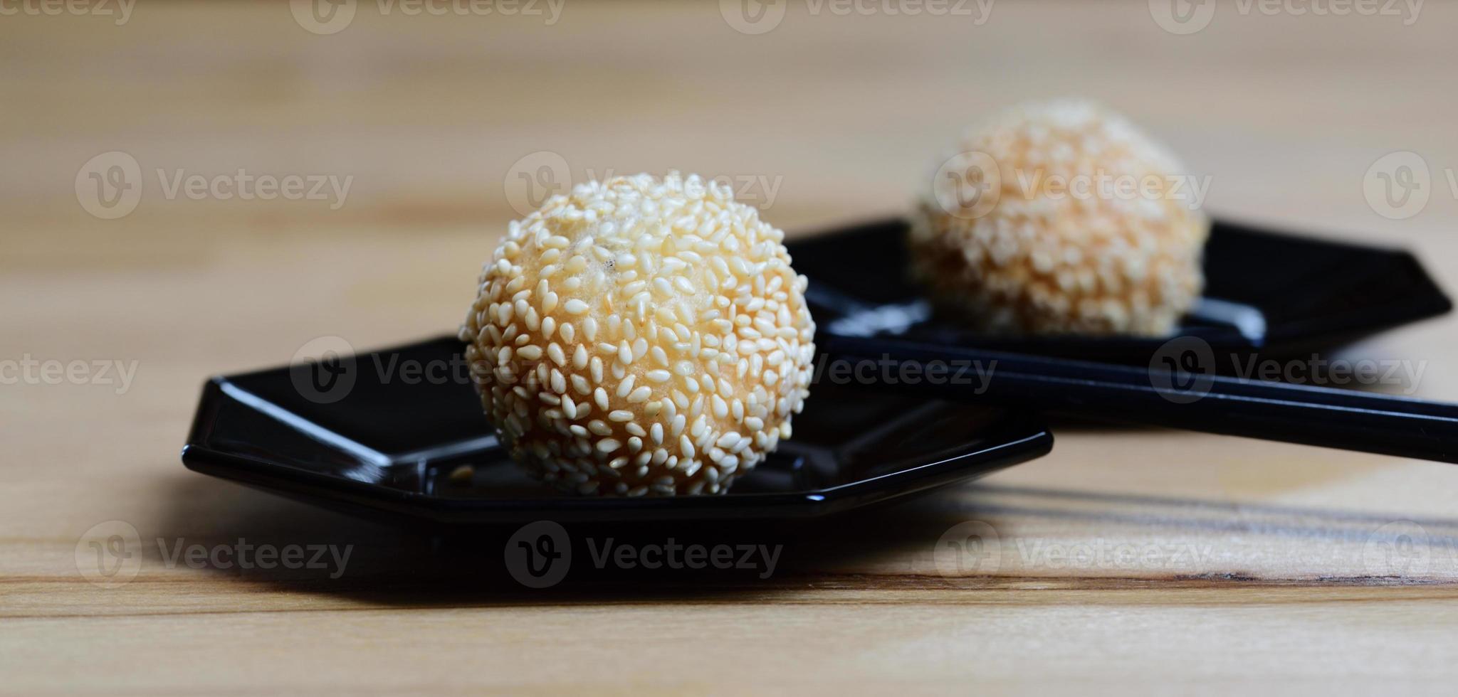 Close up of fresh deep fried sesame balls or jian dui lying on dark plates against a light background with chopsticks photo
