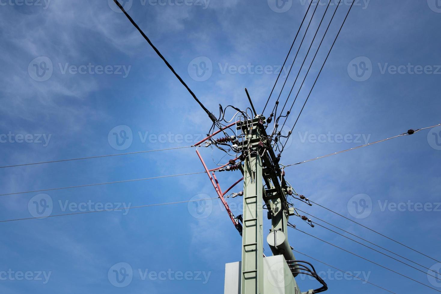A mast with a network of many different power cables is photographed from below against the blue sky with clouds photo