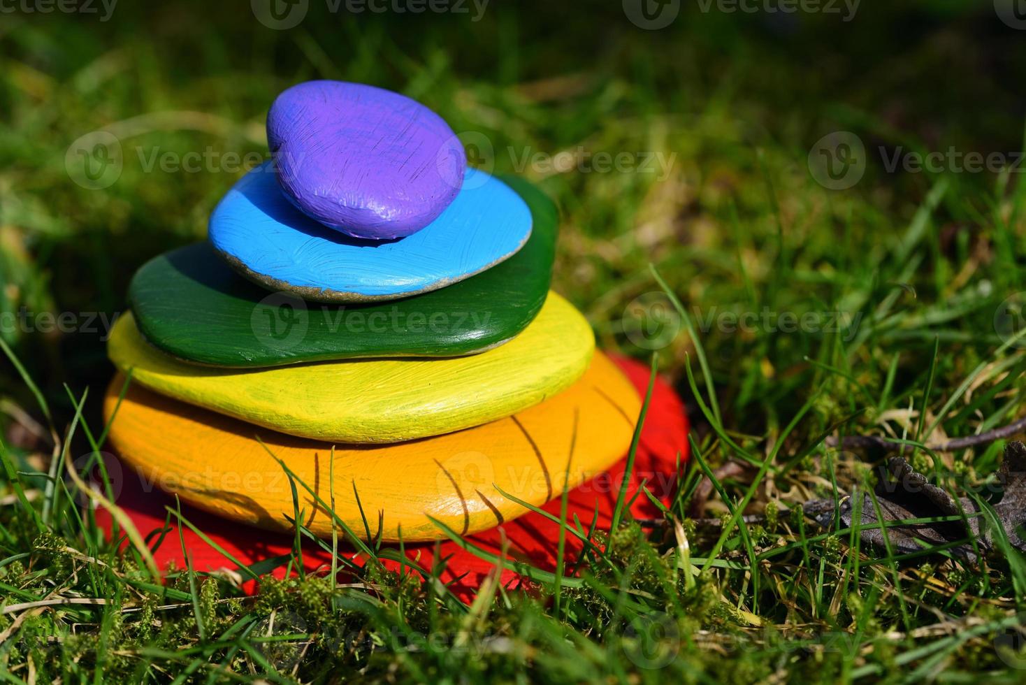Several brightly colored pebbles painted in rainbow colors lie on top of one another in a meadow with green grass photo